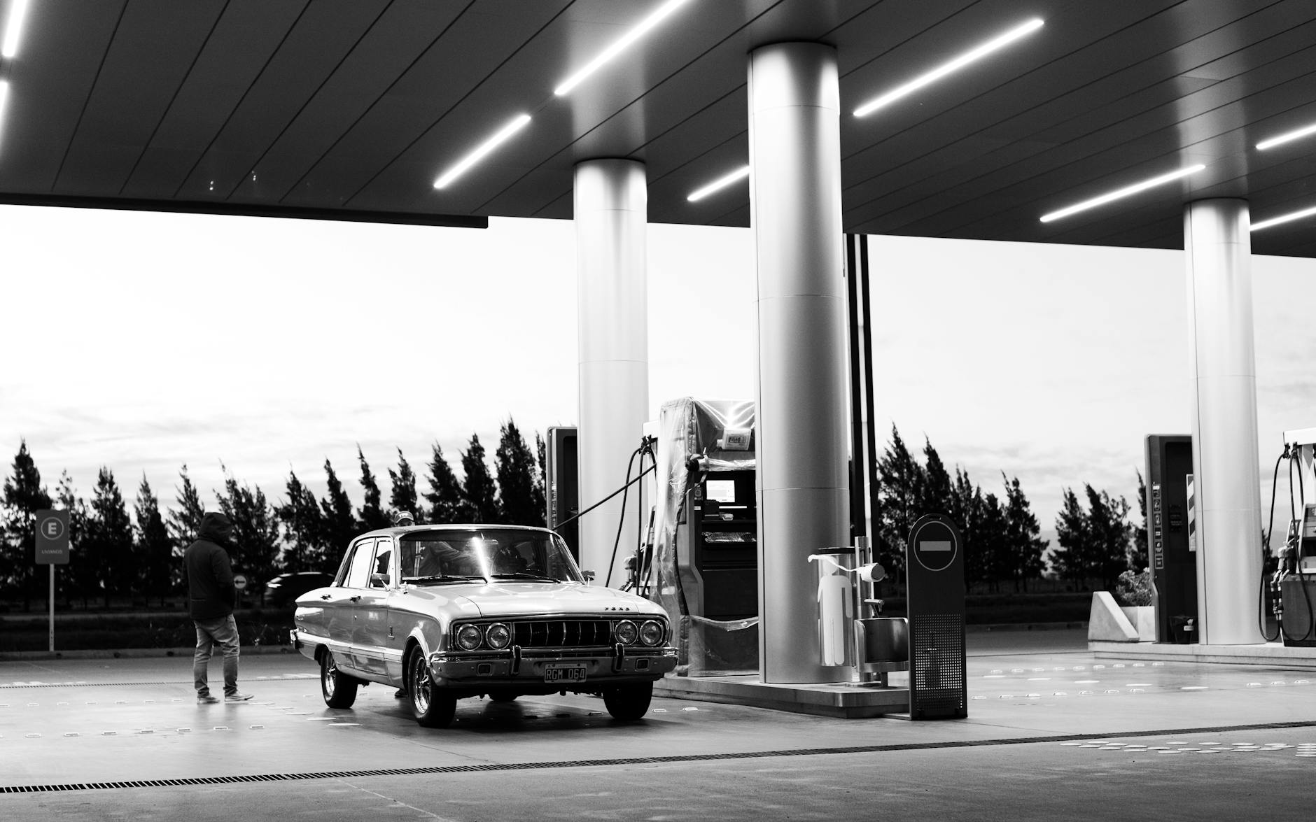 Czarno-białe zdjęcie zabytkowego samochodu przy stacji paliw