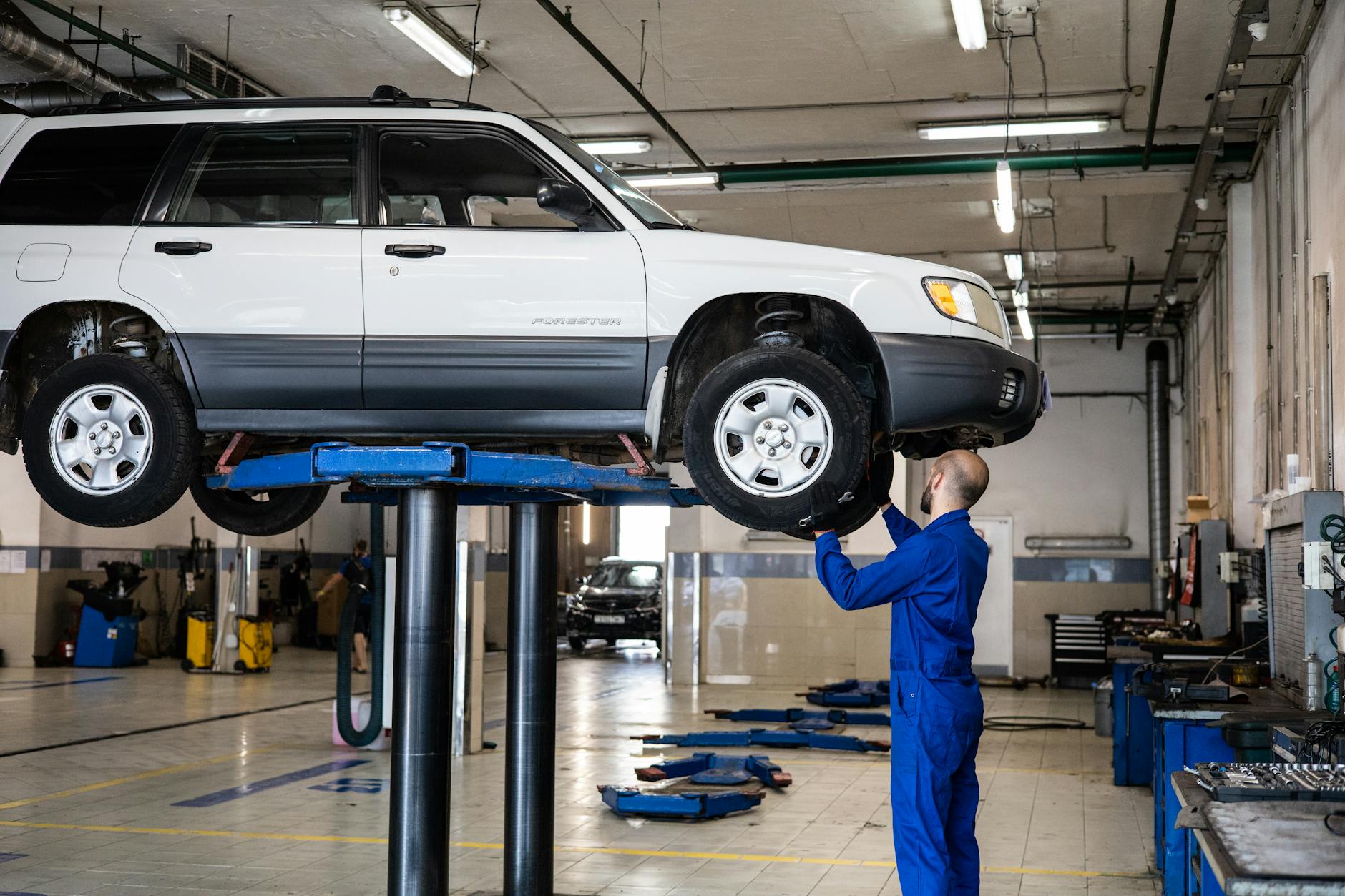 Mechanik sprawdza zawieszenie białego SUV-a na podnośniku w warsztacie