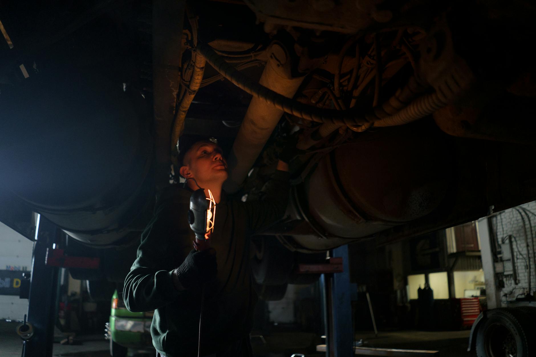 Mechanik z lampą inspekcyjną sprawdza podwozie auta w warsztacie