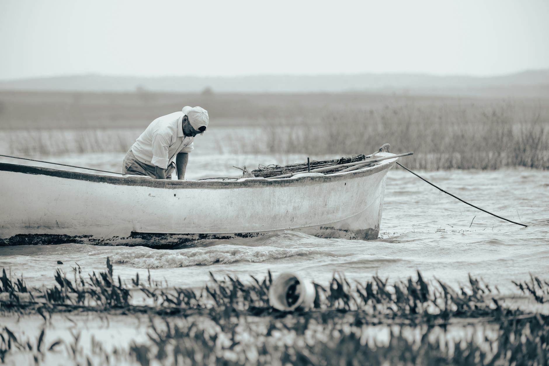 Wędkarz pochylony nad burtą białej łodzi na spokojnym jeziorze