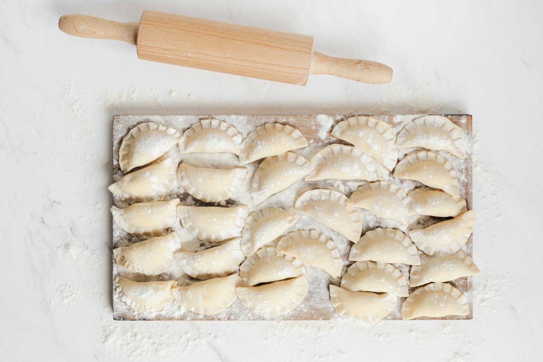 Domowe pierogi ruskie na oprószonej mąką desce z wałkiem