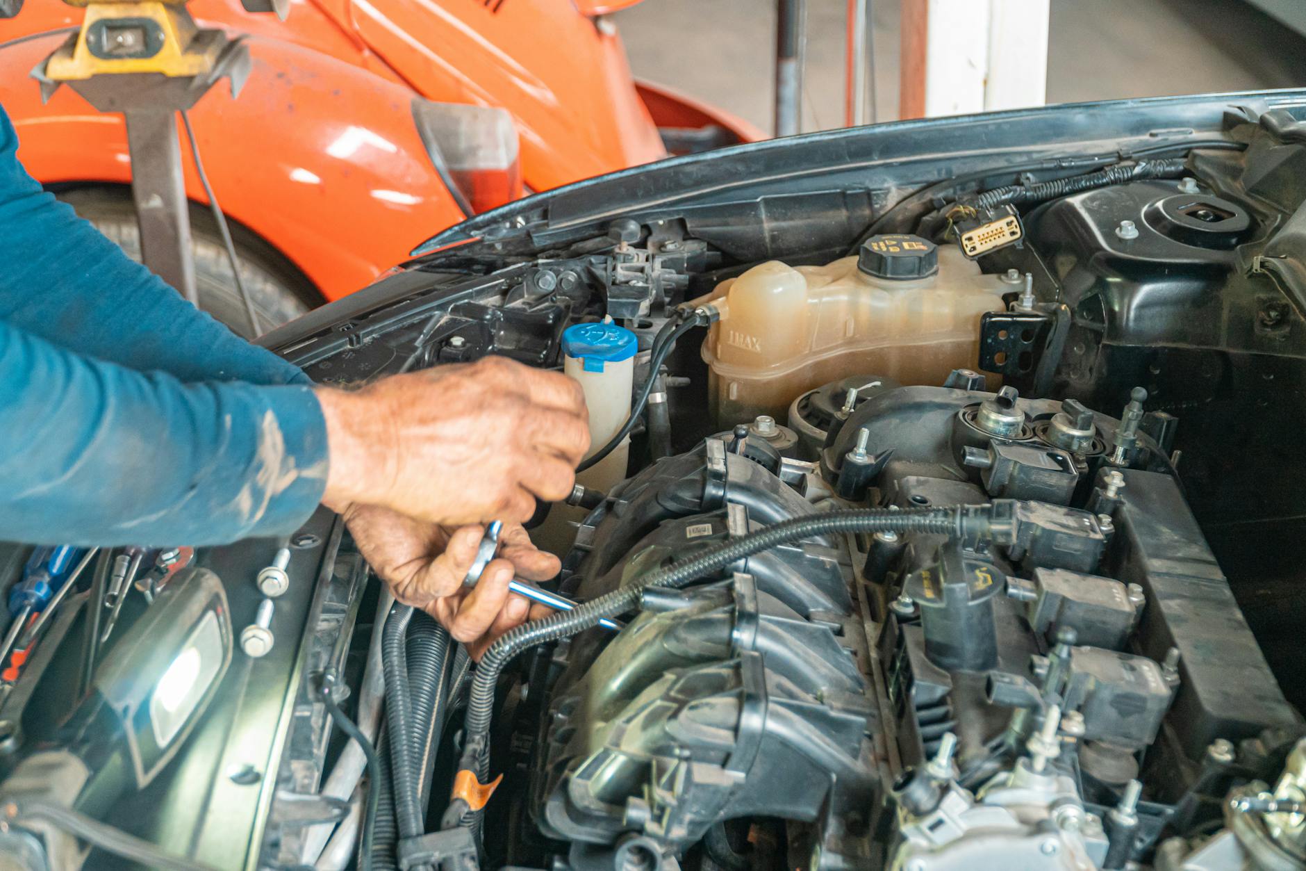 Mechanik naprawiający pod maską układ sprzęgła w samochodzie Mechanik naprawiający pod maską układ sprzęgła w samochodzie