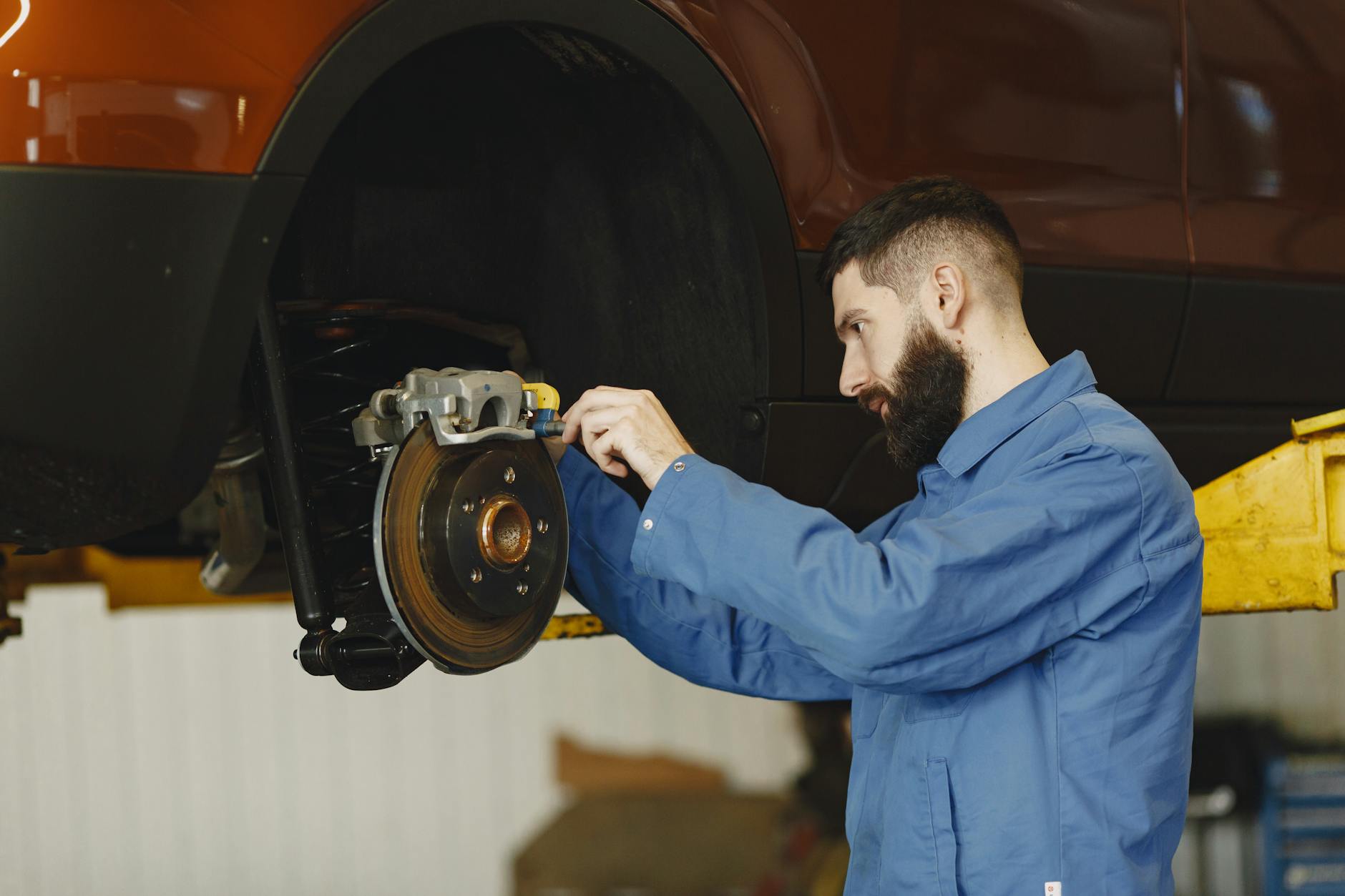 Mechanik w niebieskim kombinezonie reguluje hamulce samochodu w warsztacie