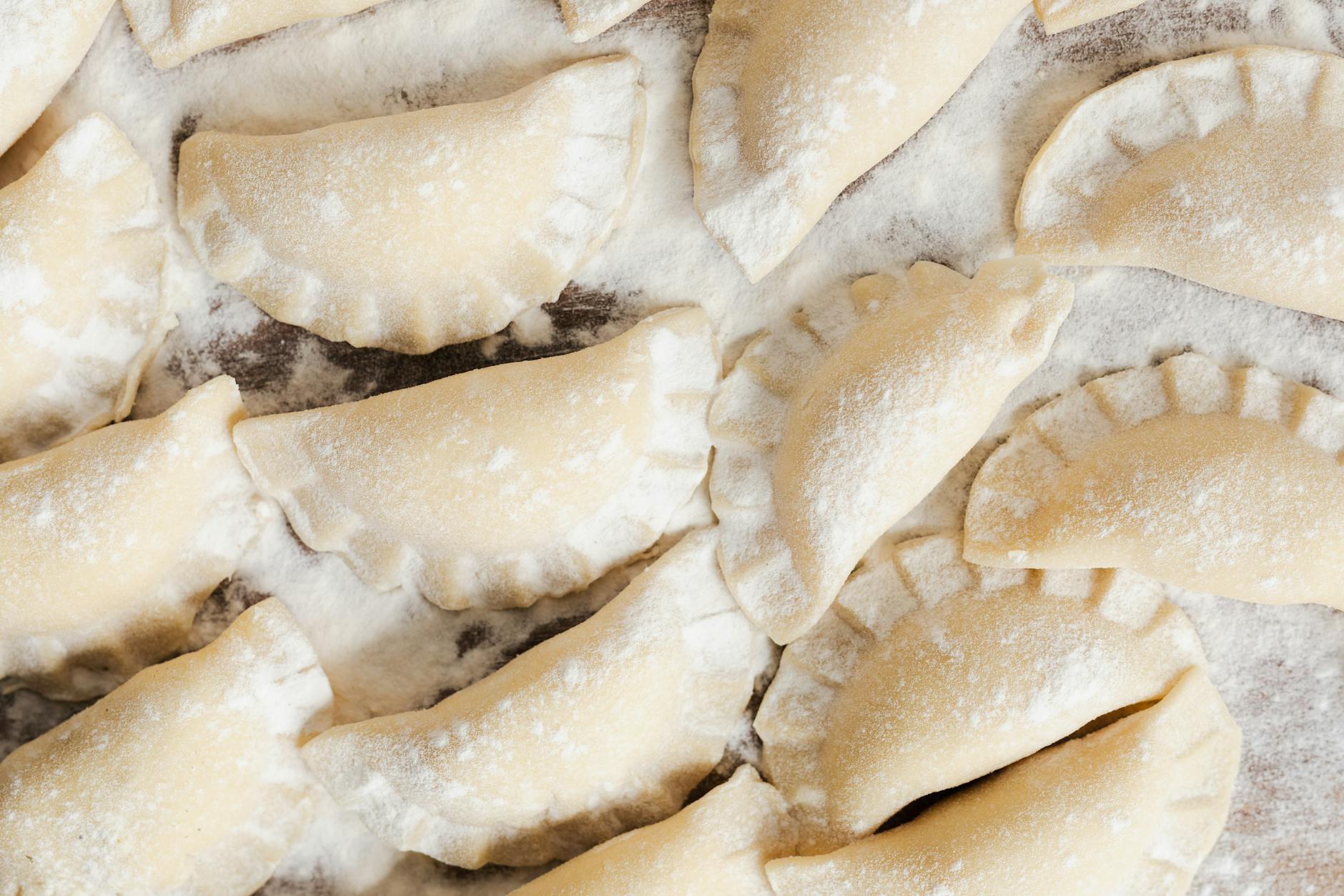 Surowe pierogi ruskie ułożone na oprószonym mąką blacie