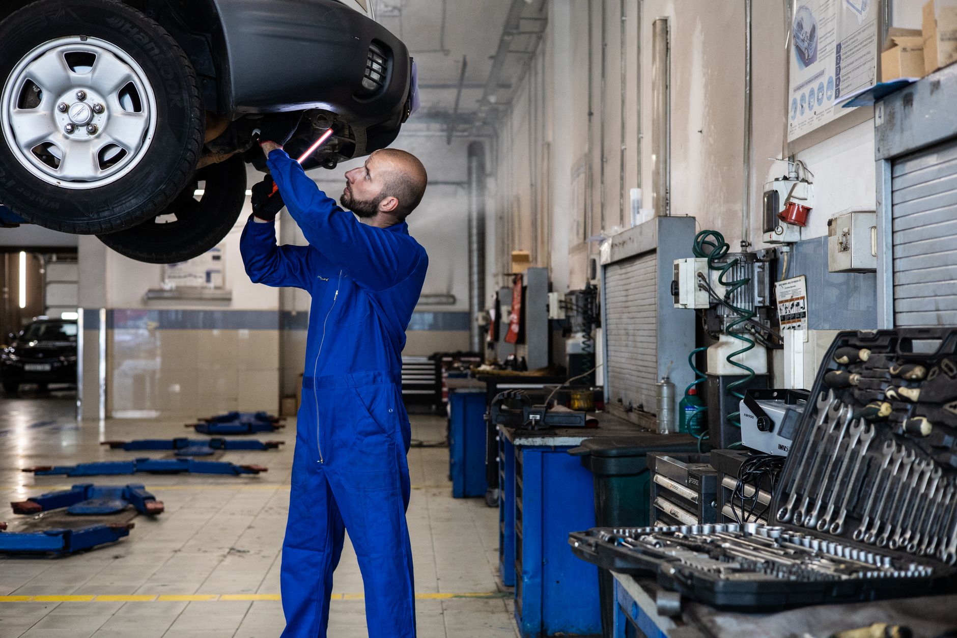 Mechanik ogląda od spodu podniesiony samochód w warsztacie samochodowym
