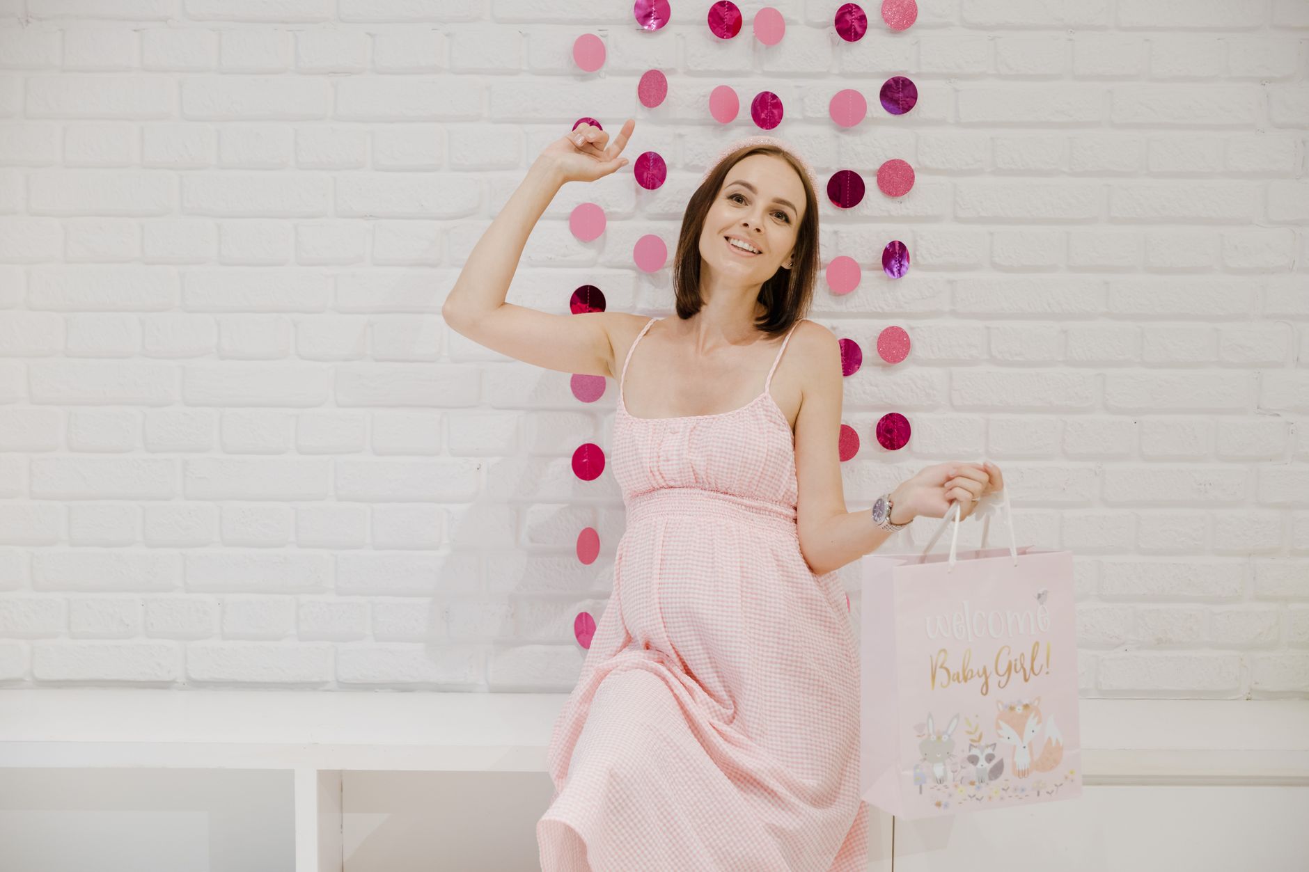Uśmiechnięta kobieta w ciąży w różowej sukience na baby shower indoors