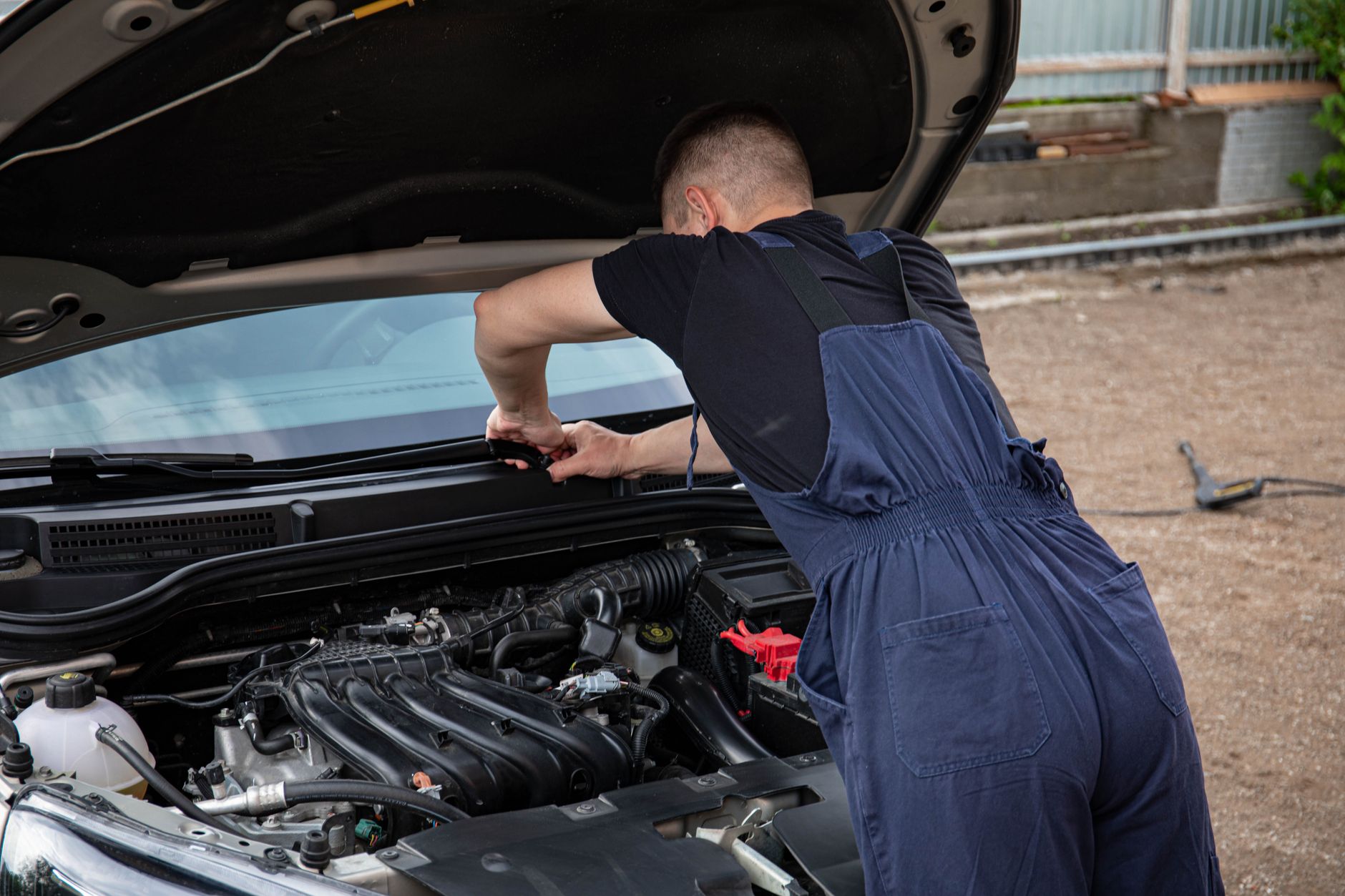 Auto gaśnie na dziurach: jak znaleźć przerwę w zasilaniu pompy paliwa Mechanik naprawia silnik samochodu na zewnątrz latem